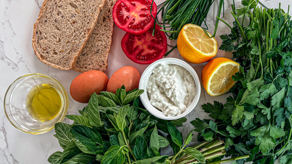 basil, chives, parsley, lemons, eggs, sourdough, olive oil whipped cottage cheese toast flat lay.