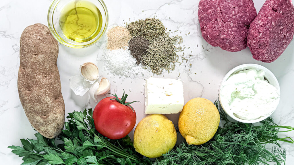 zesty Mediterranean burger with lemon herb fries ingredients flat lay: russet potato, olive oil, salt, pepper, thyme, oregano, garlic salt, ground beef, Greek Yogurt, feta, lemon, parsley, dill, and tomato