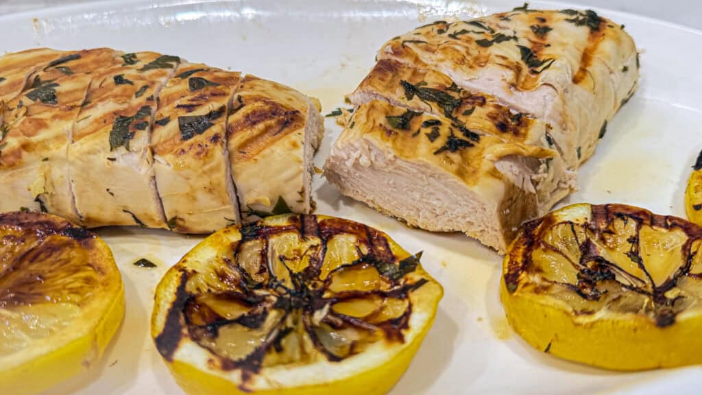 Juicy lemon herb chicken, sliced cooked chicken with parsley crust and charred lemons on a white platter