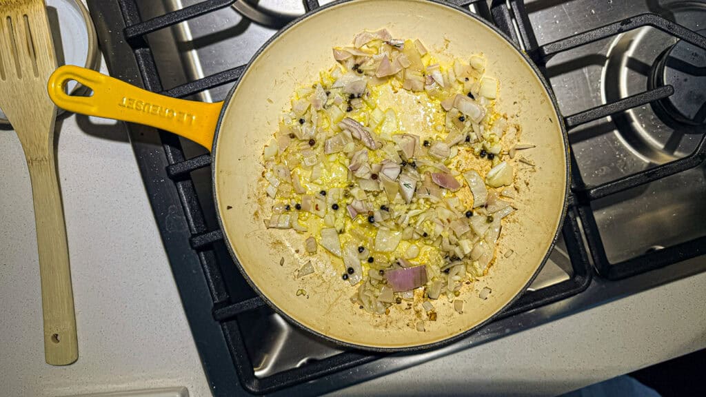 Juicy lemon herb chicken process shot, saut&eacute;ing shallots and peppercorns in a yellow frying pan