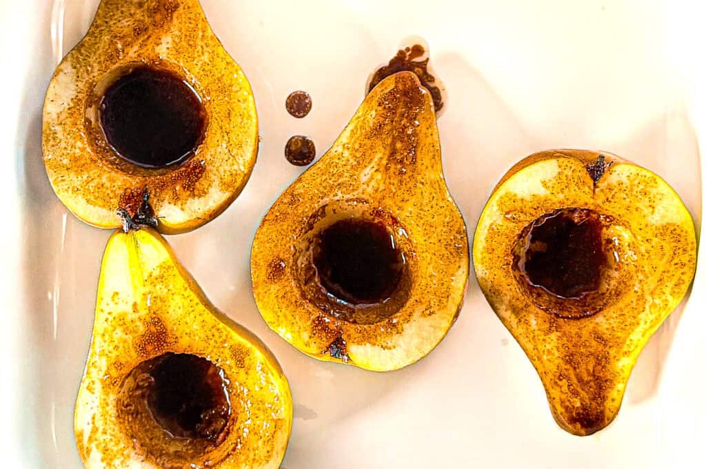 Maple Olive Oil Bosc Pears process shot, cut Bosc pears, in maple syrup in a white baking dish ready to be baked.