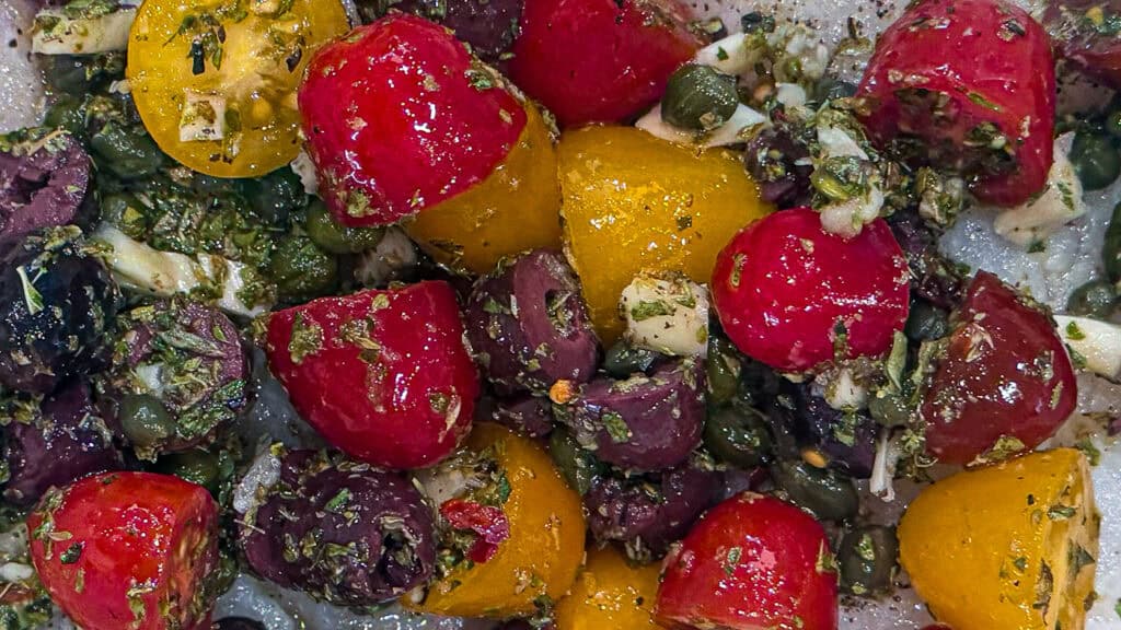 cherry tomatoes, Greek oregano, garlic, capers, olives, and olive oil in a bowl.