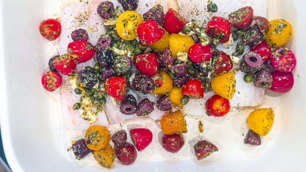 tomatoes, capers, olives, olive oil, Greek oregano, and garlic over cod in a baking dish before going into the oven.