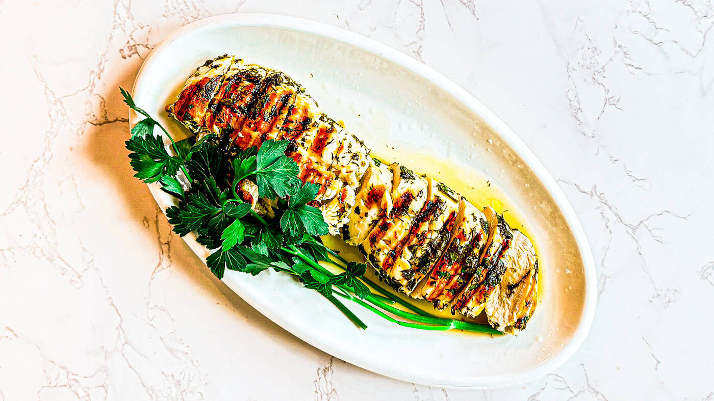 Juicy grilled lemon herb chicken breast with fresh herbs and lemon slices.