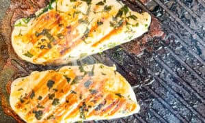 Grilled lemon herb chicken breasts with herbs on a barbecue grill.
