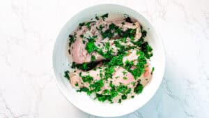 Herb-marinated chicken breast garnished with fresh parsley in a white bowl.