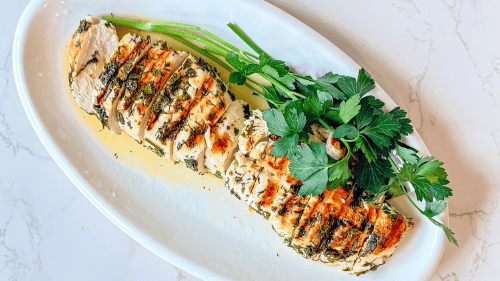Juicy lemon herb chicken lifestyle shot, parsley crusted chicken breast with lemon marinade on a white platter, with parsley on a white marble surface
