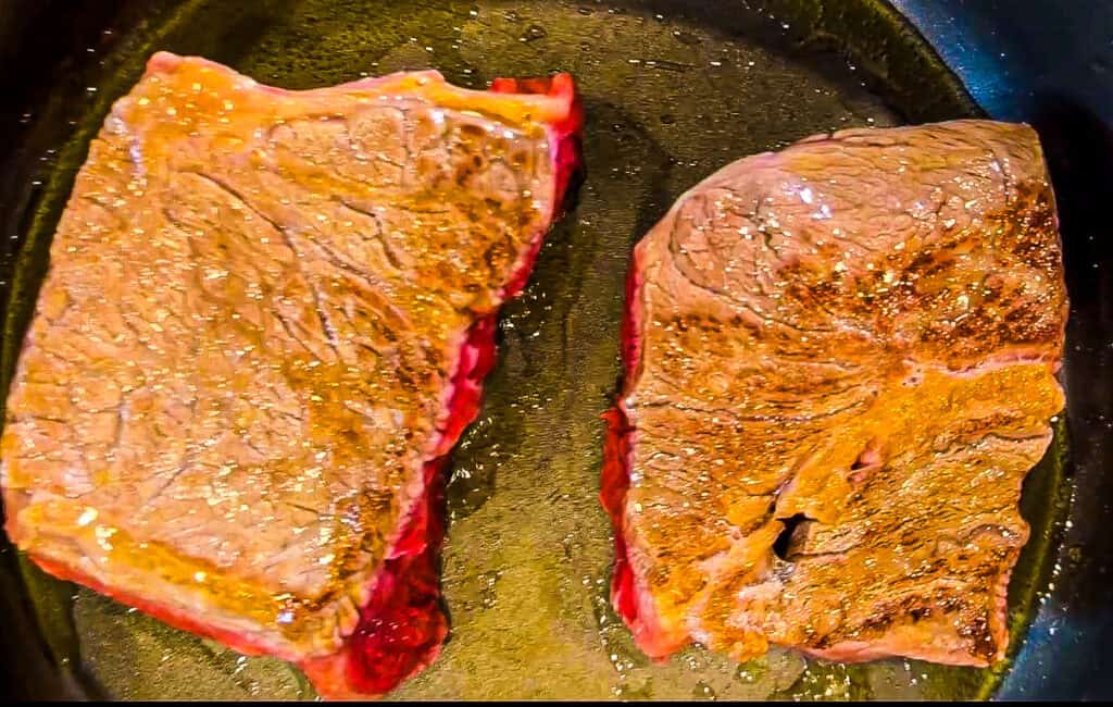 Two seared beef pot roast pieces in a skillet, ready for cooking.
