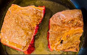 Two seared beef pot roast pieces in a skillet, ready for cooking.