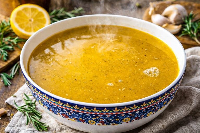 Fresh homemade chicken broth in a decorative bowl with herbs and lemon.