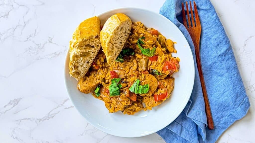 Braised Chicken Sausages with Peppers in. a white bowl with French bread.