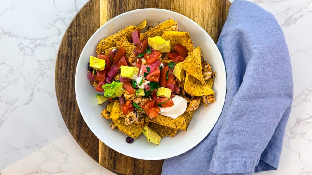Mediterranean chicken nachos in a bowl on a cutting board