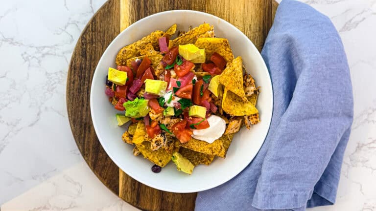 Delicious Mexican nachos topped with guacamole, salsa, and cheese on a white plate.