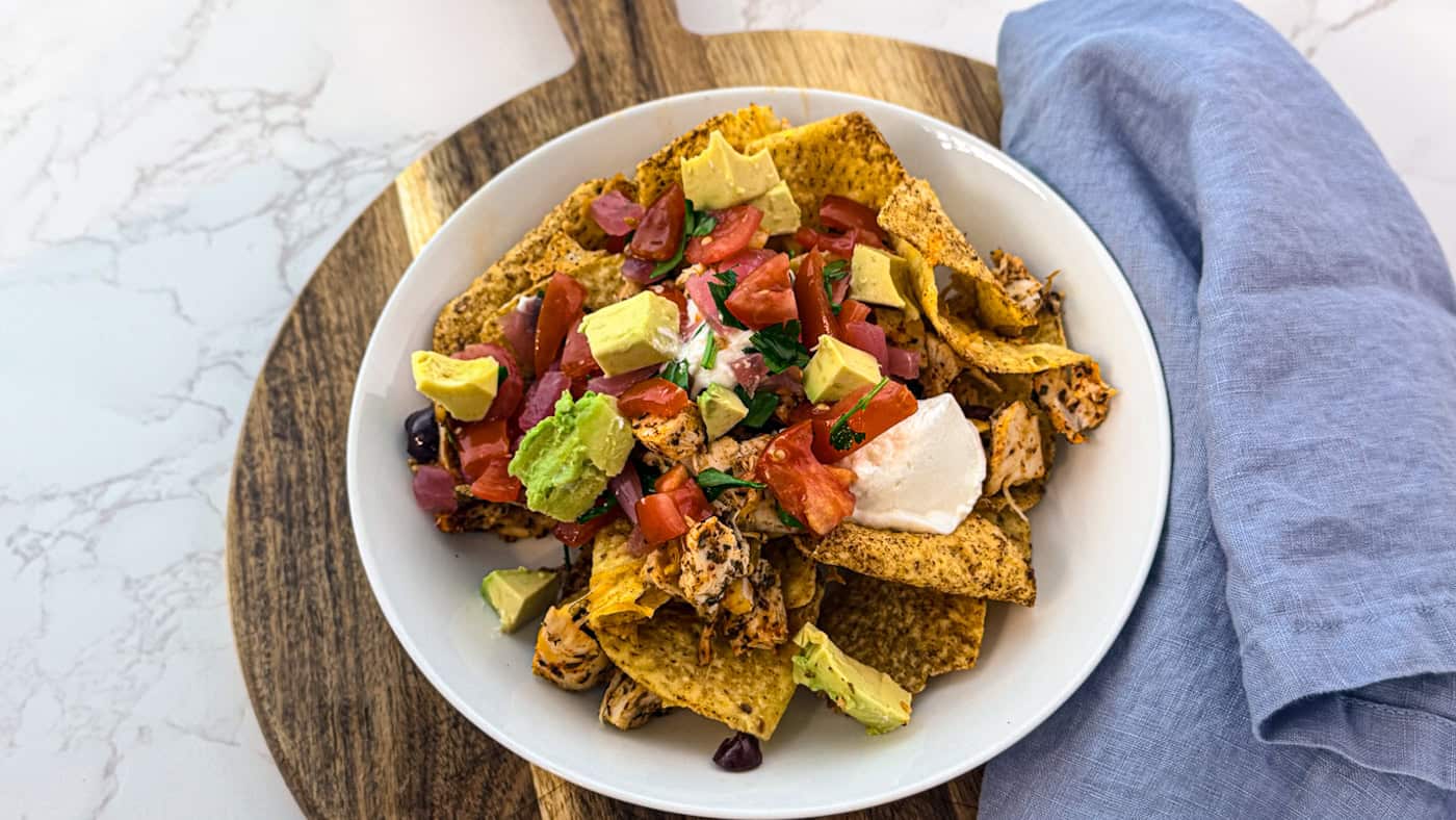 Crispy nachos topped with guacamole, salsa, and sour cream on a white plate.
