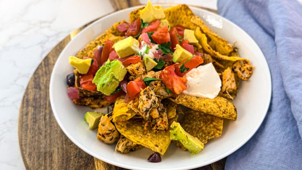 sheet pan chicken nachos in a white bowl on a cutting board with a. blue linen napkin