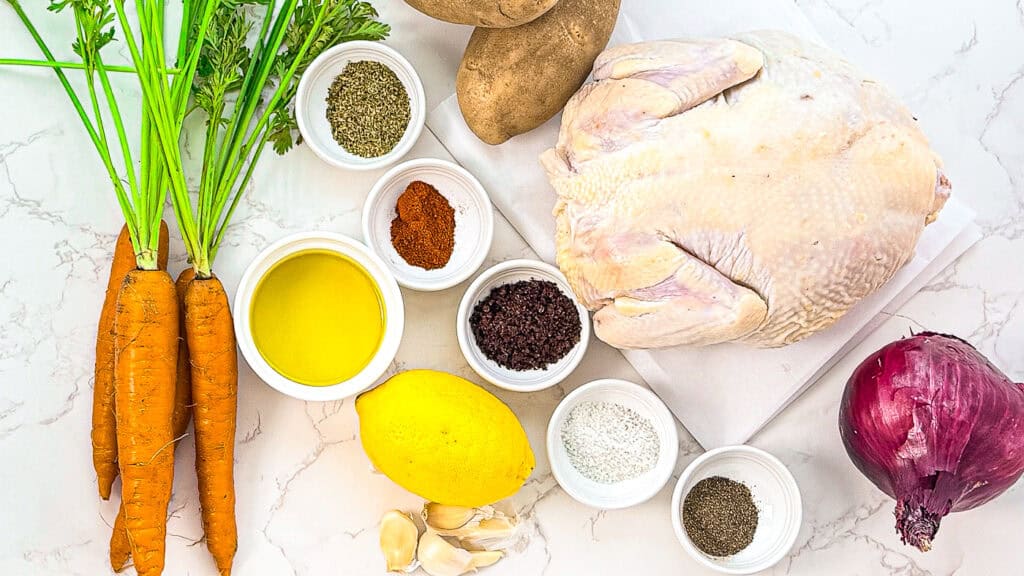 Easy Sumac Roasted Whole Chicken, ingredients flat lay with carrots, lemon, garlic, red onion, whole chicken, potatoes, oregano, pepper, salt, paprika, sumac, lemon, olive oil