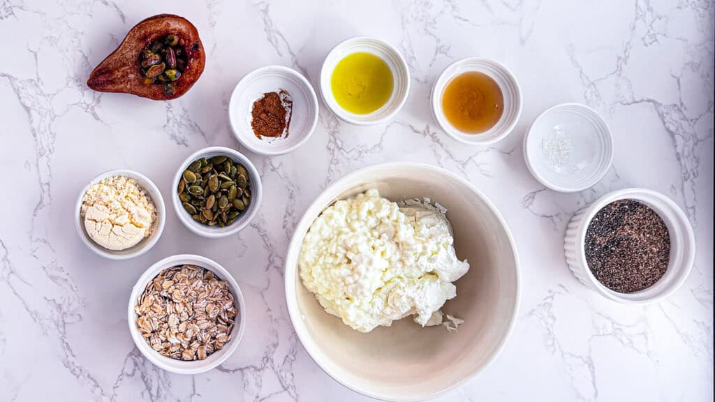 homemade olive oil ingredients flat lay with yogurt, cottage cheese, seeds, salt, maple syrup, olive oil, cinnamon, pumpkin seeds, oats, Bosc pears