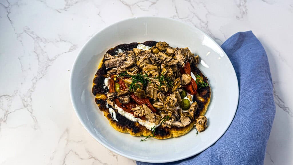 Chicken thigh flatbreads in a bowl with a blue linen napkin on a white marble surface