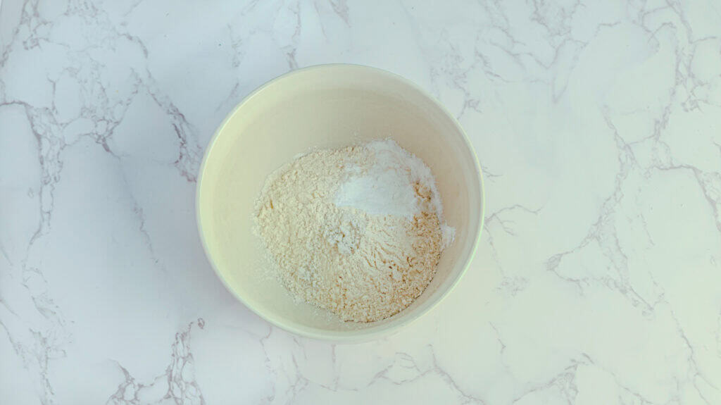 Fresh baking flour in a white bowl on marble surface.