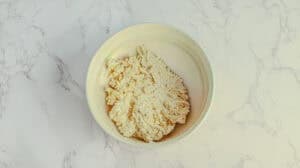Dough in a white bowl on marble surface, ready for baking or cooking.
