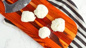 Fresh ricotta cheese balls displayed on a wooden cutting board for homemade Italian recipes.