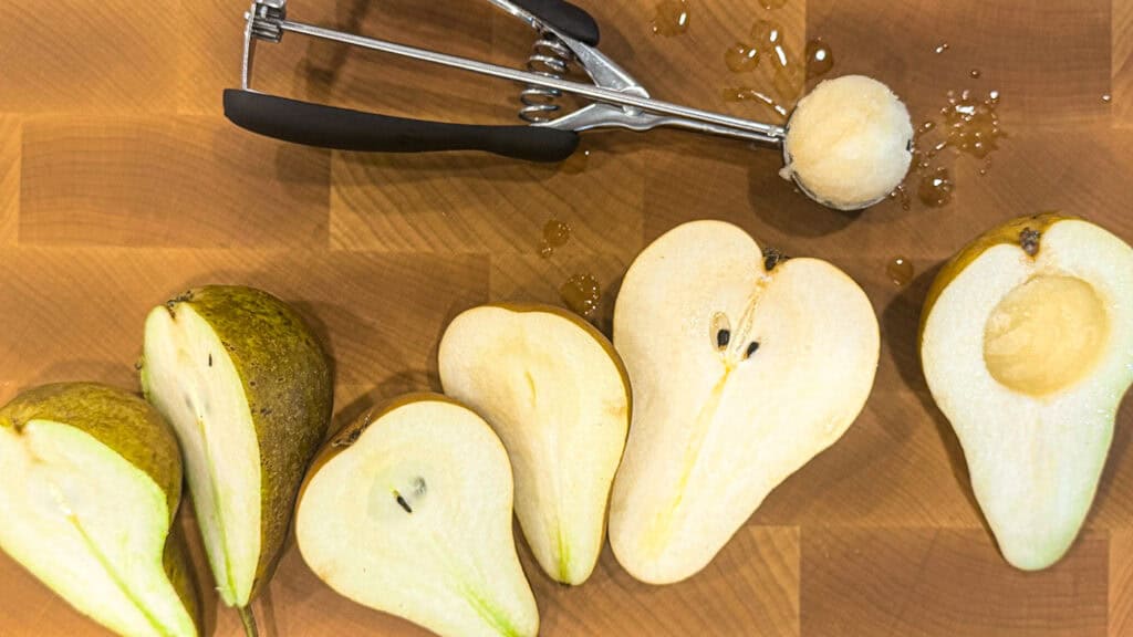 Sliced pears on a wooden cutting board with a melon baller tool.