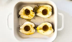 Baked Bosc pears halved with olive oil and spices in a white baking dish.