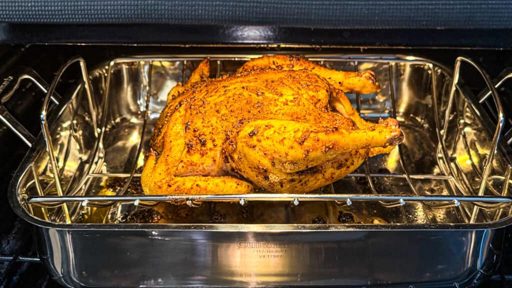 raw chicken with sumac, lemon zest, paprika, garlic, and olive oil rubbed on it sitting in a metal baking pan sitting in the oven.