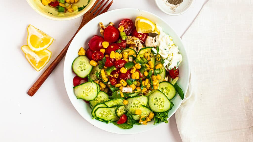 Fresh vegetable salad with cucumbers, cherry tomatoes, corn, and herbs.