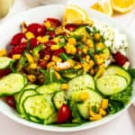 Fresh corn and cucumber salad with cherry tomatoes, herbs, and lemon wedges for a healthy, refreshin.