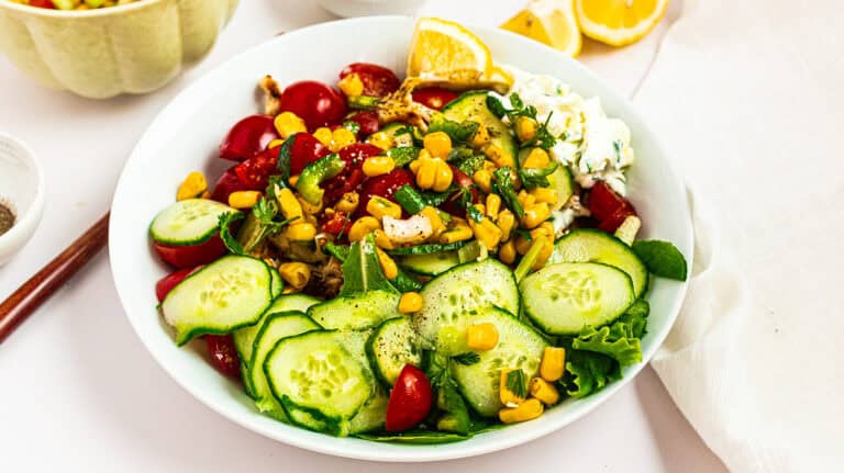 Fresh corn and cucumber salad with cherry tomatoes, herbs, and lemon wedges for a healthy, refreshin.
