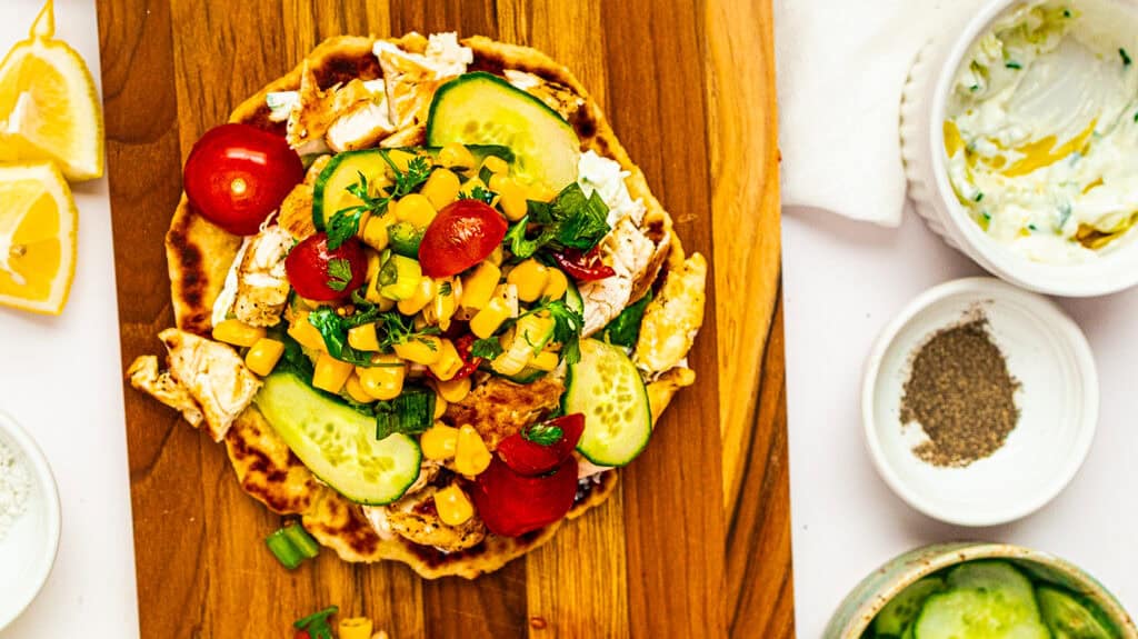 Delicious chicken tacos topped with fresh vegetables, corn, and salsa on a wooden serving board.