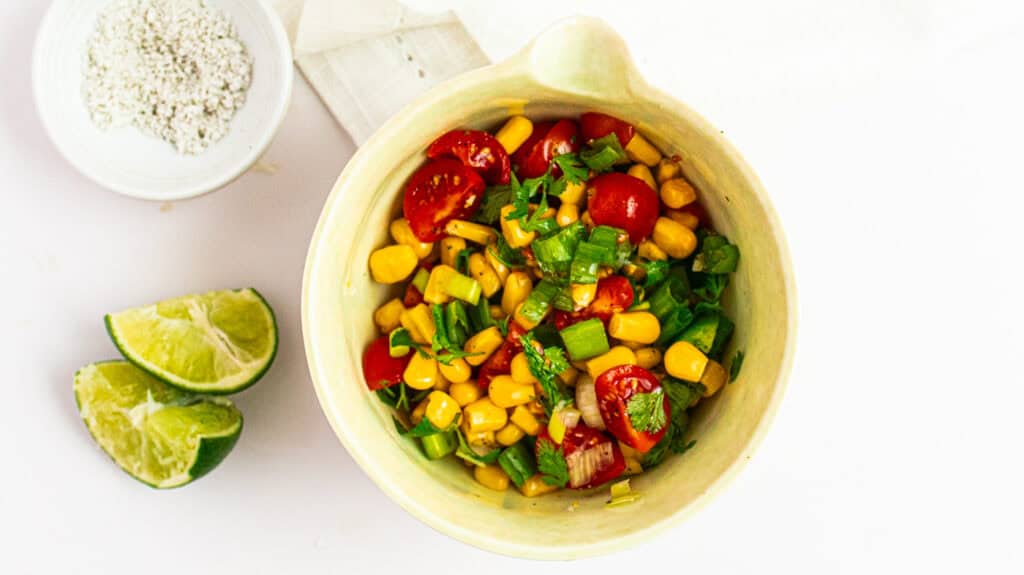 Fresh corn and cherry tomato salad with chopped green onions, served with lime wedges for added flav.