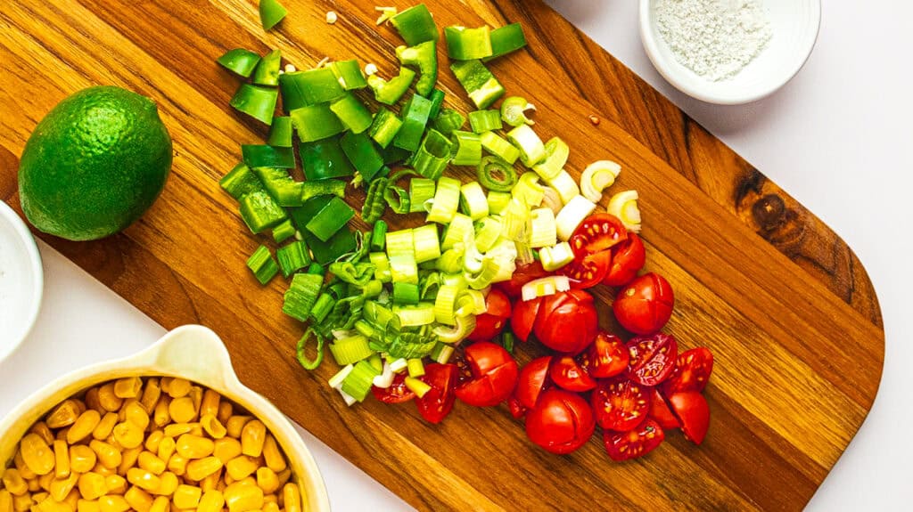 Fresh chopped green onions, cherry tomatoes, and corn on a wooden cutting board for healthy cooking.