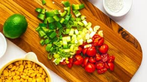 Fresh chopped green onions, cherry tomatoes, and corn on a wooden cutting board for healthy cooking.
