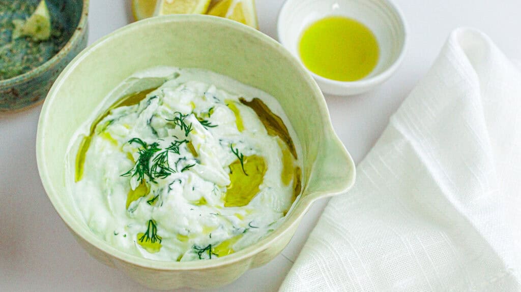 Creamy tzatziki sauce garnished with dill and olive oil in a green bowl.
