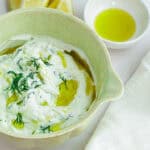 Creamy tzatziki sauce garnished with dill and olive oil in a green bowl.