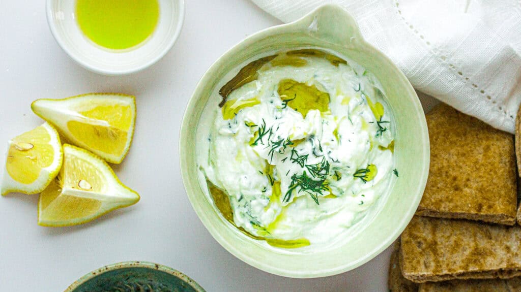 Creamy tzatziki dip garnished with dill, served with lemon wedges and pita bread.