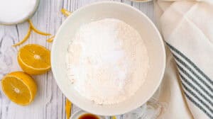 Flour in a white bowl with lemon halves and baking ingredients.