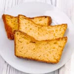 Slices of lemon orange olive oil loaf cake on a white plate with a lemon wedge and gold fork.