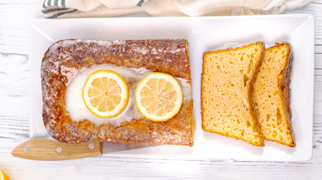 Slice of lemon orange olive oil loaf cake with lemon slices on top.