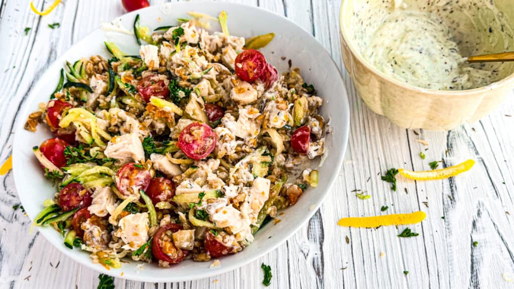 Mediterranean chicken salad with farro in a white bowl with a white linen napkin on a wooden board