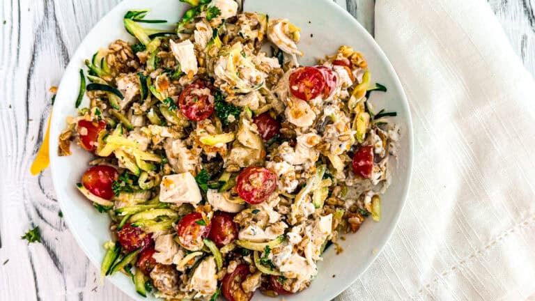 Mediterranean chicken salad with farro in a white bowl with a white linen napkin on a wooden board