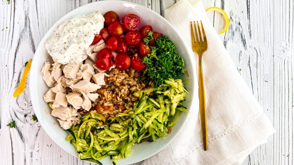 Healthy chicken salad with cherry tomatoes, greens, and grains on a white plate.