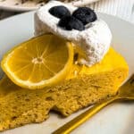 Lemon cake slice topped with blueberries, lemon slice, and whipped cream.