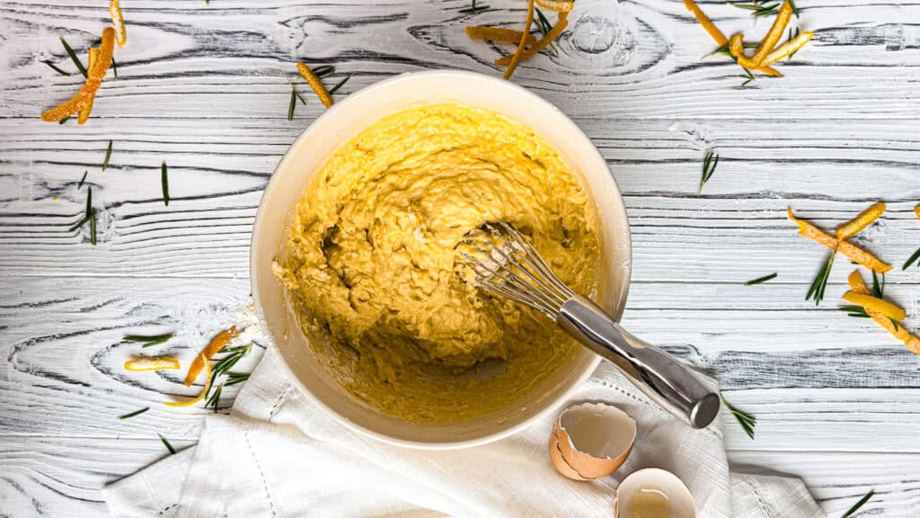 Creamy lemon batter in a white bowl with a whisk, on a rustic wooden surface.
