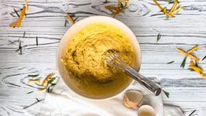 Creamy lemon batter in a white bowl with a whisk, on a rustic wooden surface.