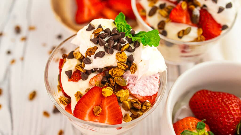 Delicious parfait with strawberries, whipped cream, and chocolate chips in a glass.