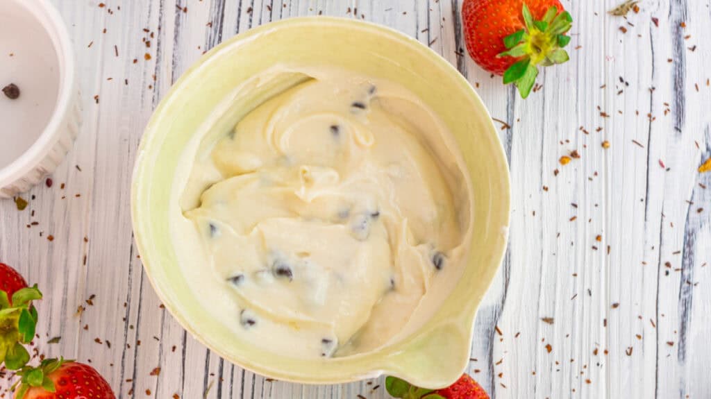 Creamy vanilla strawberry rose parfait in a bowl with strawberries nearby.