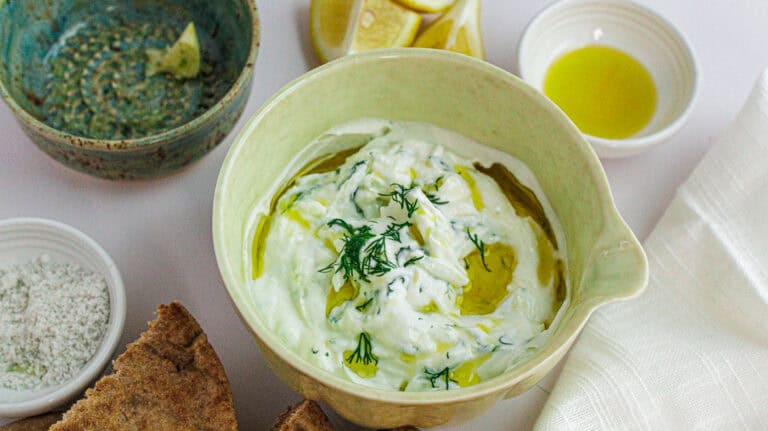 Creamy tzatziki dip garnished with herbs, olive oil, and served with bread slices.